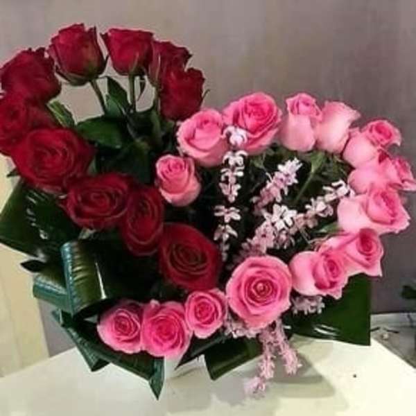 Heart-shaped bouquet of red and pink roses with small white filler flowers