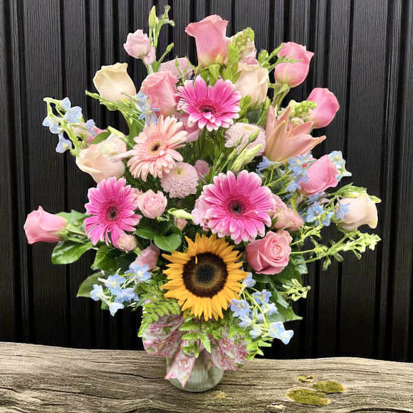 Tall mixed bouquet of pink roses and gerbera daisies with a sunflower in a glass vase
