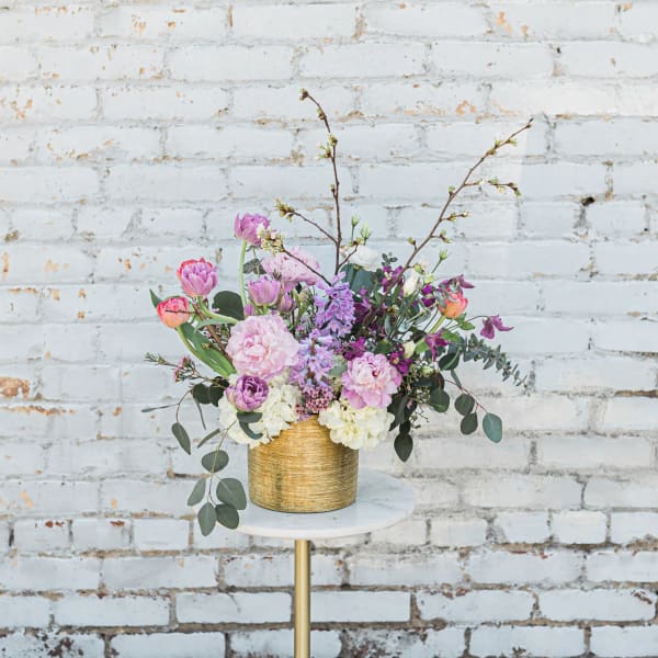 Pastel floral arrangement in a gold vase on a small round table