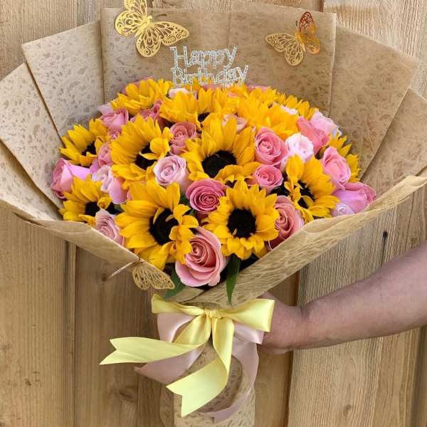 Bouquet of yellow sunflowers and pink roses with a birthday topper