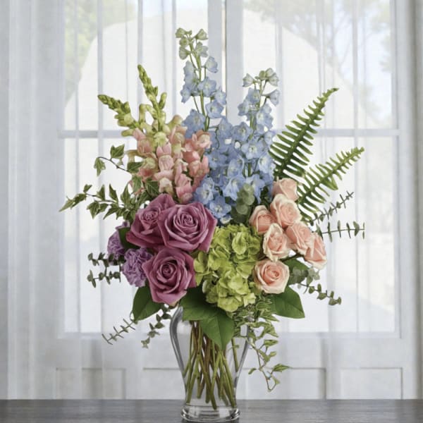 Mixed bouquet of roses, hydrangeas, and blue delphinium in a glass vase