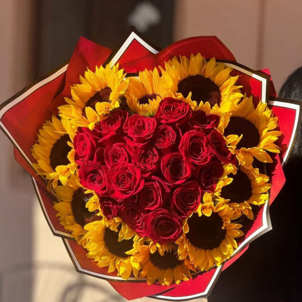 Heart-shaped bouquet of red roses and yellow sunflowers wrapped in red paper