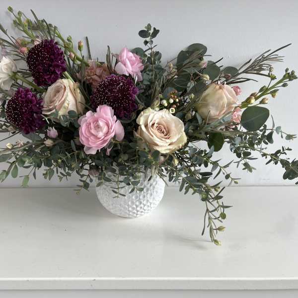 Pink and cream roses with dark purple blooms in a white vase