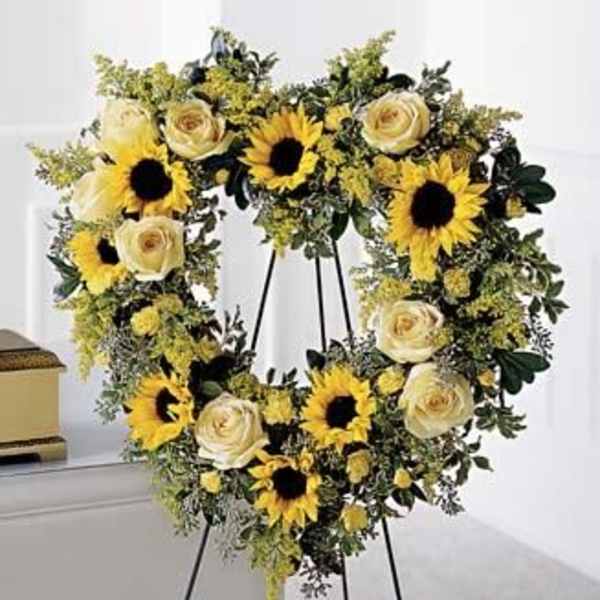 Round wreath of yellow sunflowers and ivory roses on a black easel stand