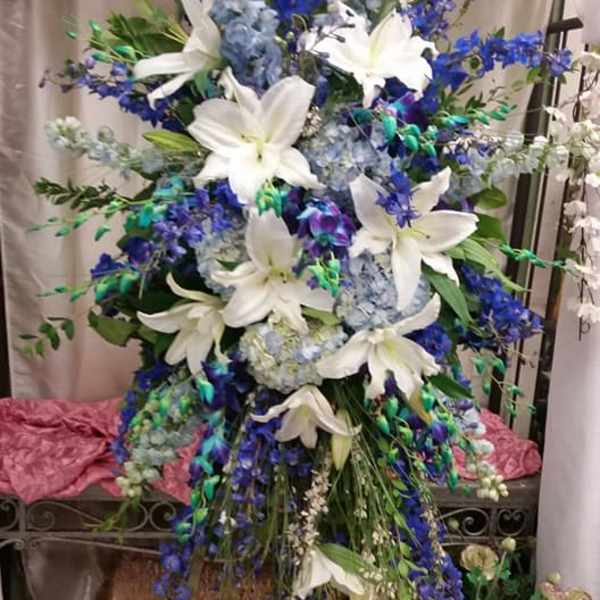 Tall floral spray with white lilies and blue flowers on a stand