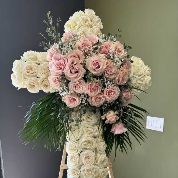 Large cross-shaped floral arrangement of white and pink roses on an easel