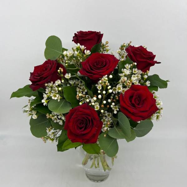 Small arrangement of red roses with tiny white filler blooms in a clear glass vase
