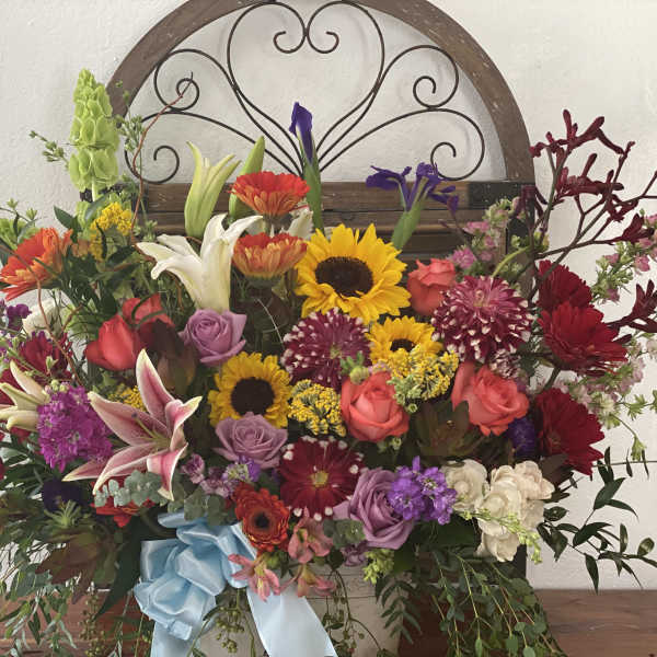 Large mixed flower arrangement with sunflowers, roses, lilies, and a blue ribbon