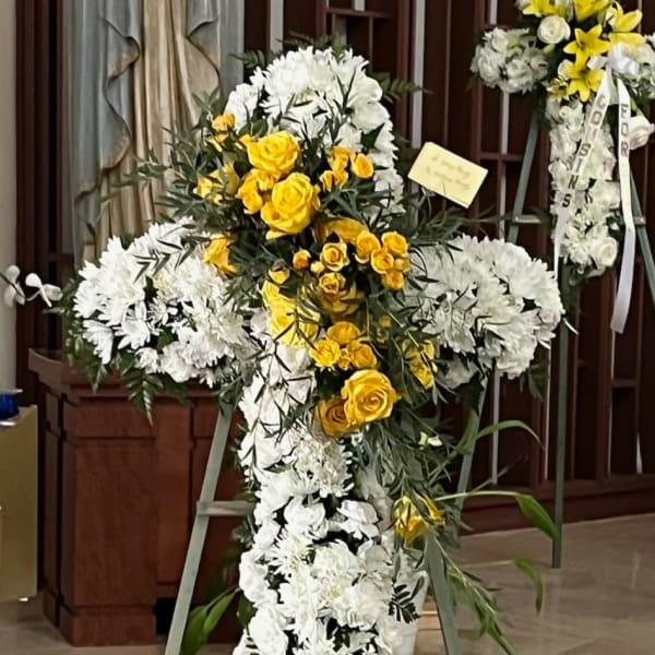Cross-shaped floral standing spray with white and yellow flowers on an easel