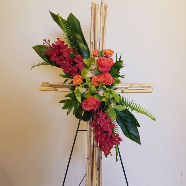 Floral cross arrangement with pink roses and red orchids on a bamboo stand