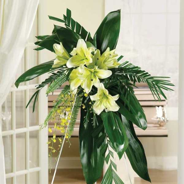 Standing floral spray with pale yellow lilies and tropical leaves