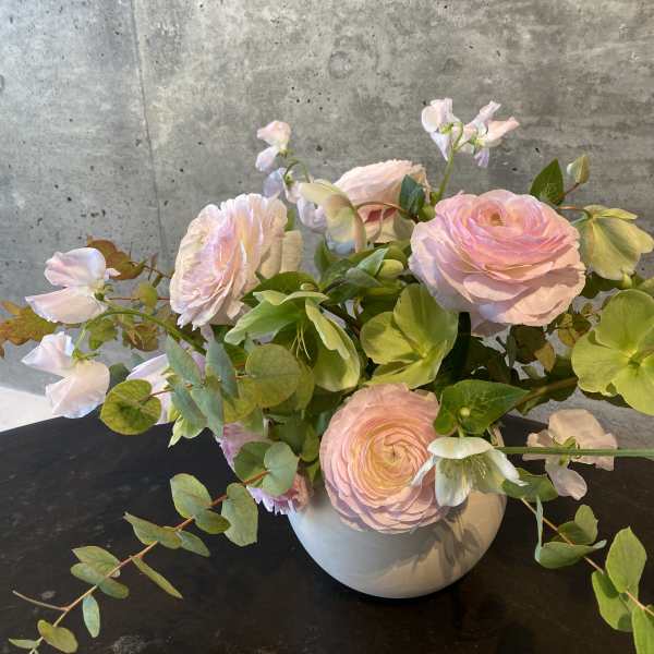 Blush pink flowers arranged in a white vase with trailing greenery
