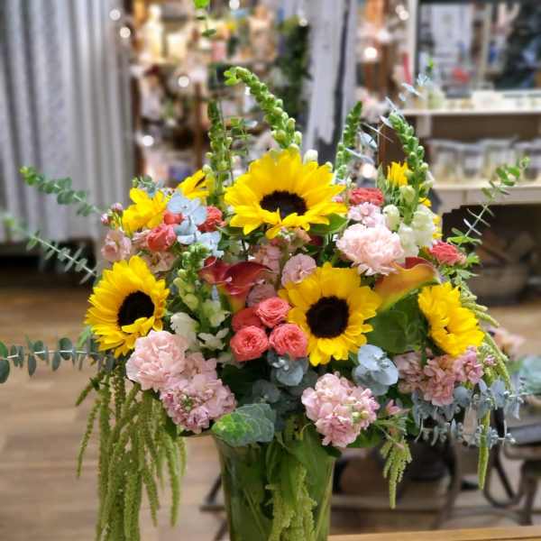 Tall mixed bouquet with sunflowers, pink blooms, and a glass vase