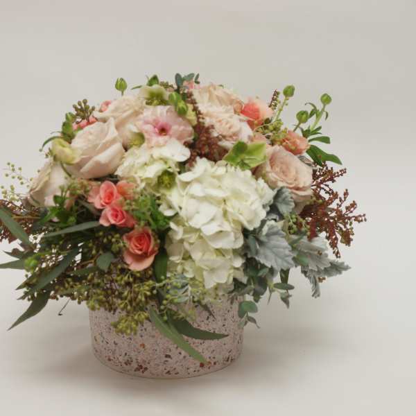 Round bouquet of blush and white flowers in a speckled box.