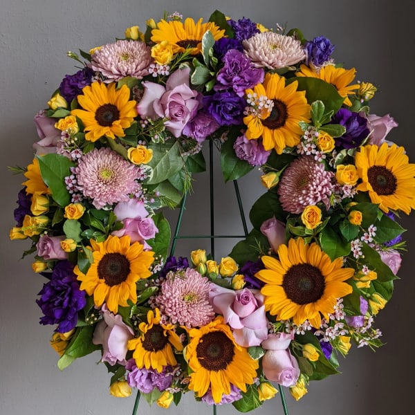 Circular wreath of sunflowers, roses, and purple blooms on a stand