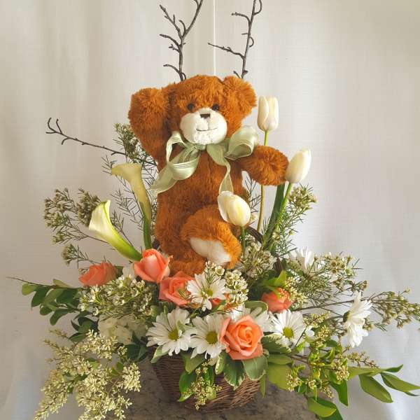 Teddy bear in a flower basket with tulips, roses, and daisies