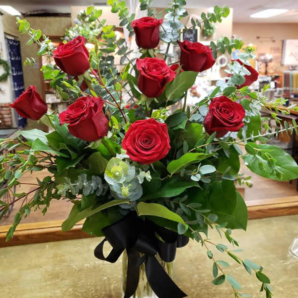 Red roses in a clear glass vase with greenery and a black ribbon