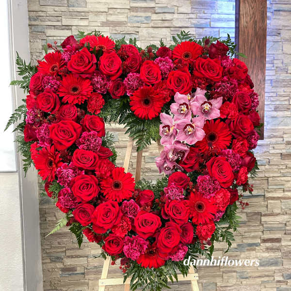 Heart-shaped floral wreath of red roses and pink orchids on an easel