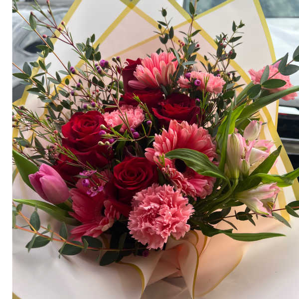 Hand-tied bouquet of red roses and mixed pink flowers wrapped in pale paper