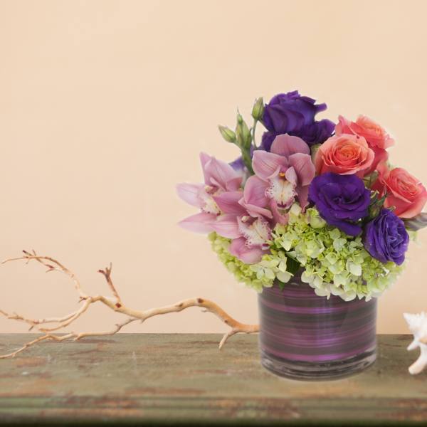 Bouquet of purple, pink, and coral flowers in a striped glass vase