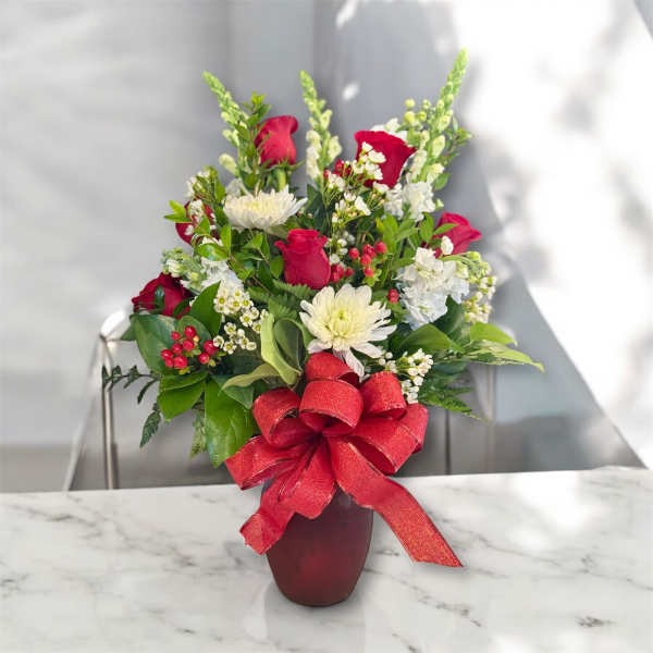 Red roses and white flowers in a vase with a red bow