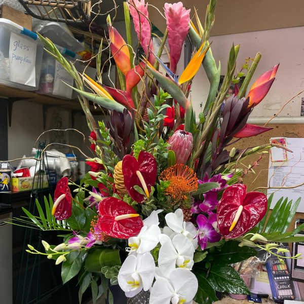 Tall tropical arrangement with orchids, anthuriums, and bird-of-paradise in a textured vase