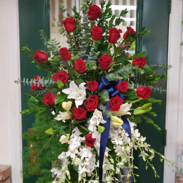 Tall floral spray with red roses, white orchids, and a blue ribbon