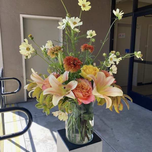 Tall mixed bouquet in a clear glass vase with lilies, roses, and daisies