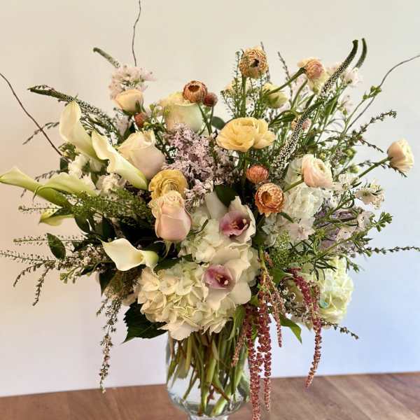 Tall arrangement of white hydrangeas, calla lilies, and pastel roses in a clear glass vase