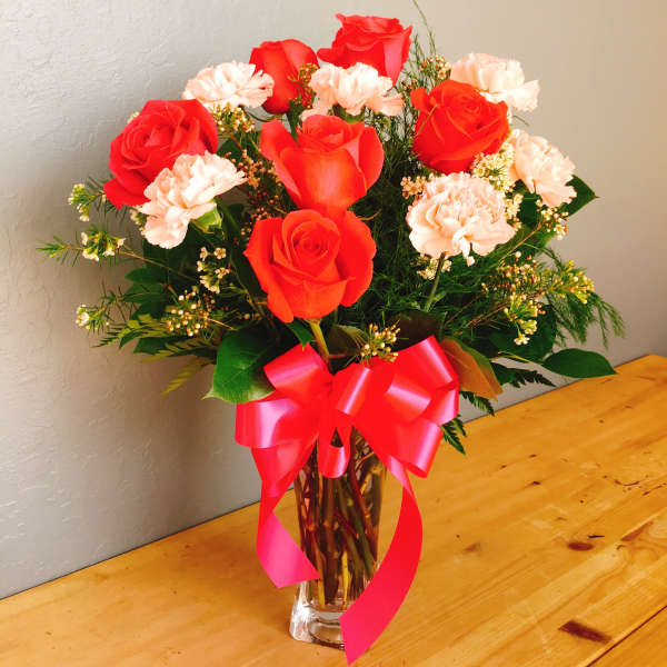 Red roses and pale pink carnations in a clear vase with a pink ribbon