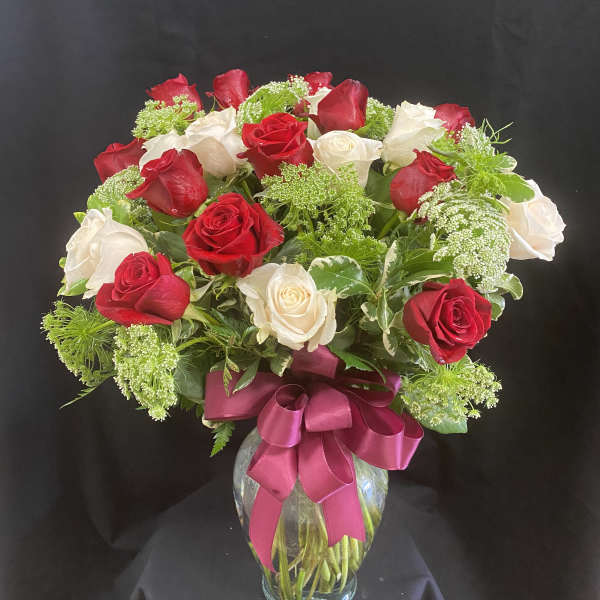 Red and white roses in a glass vase with a pink ribbon