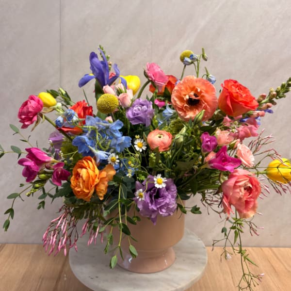 Colorful mixed flower arrangement in a blush ceramic vase on a marble stand
