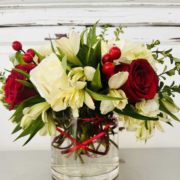 Red and white flower arrangement in a clear glass vase with a red ribbon