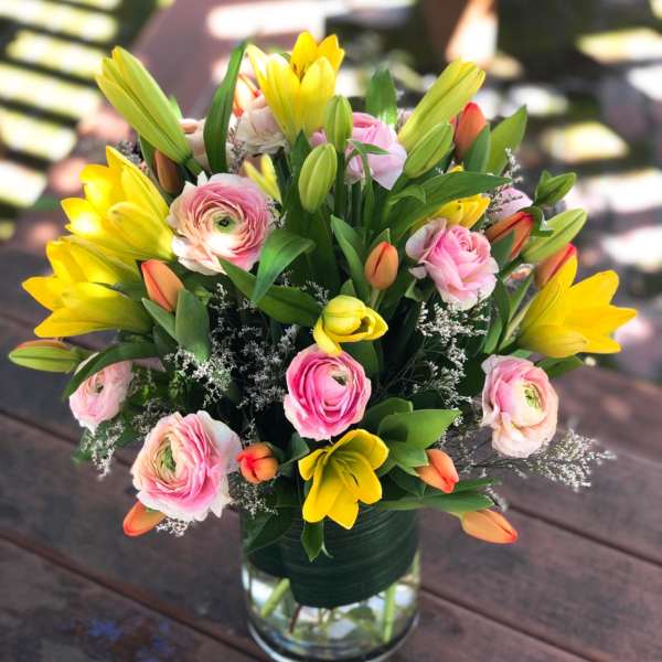Bouquet of yellow lilies and pink ranunculus in a clear glass vase