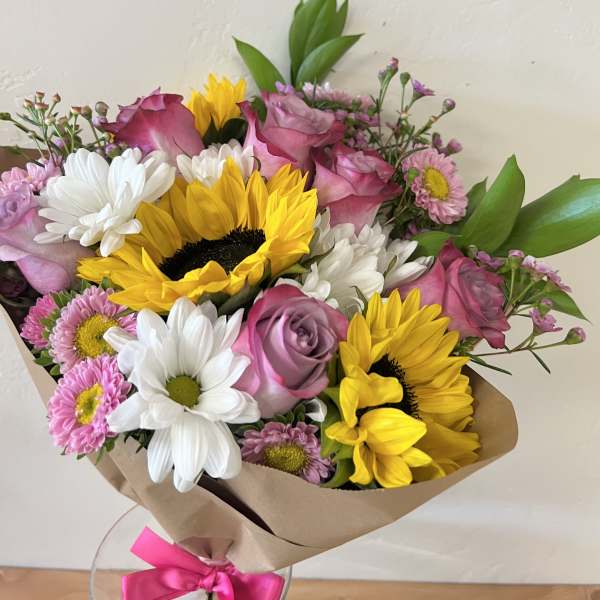 Bouquet of pink roses, sunflowers, and white daisies wrapped in brown paper