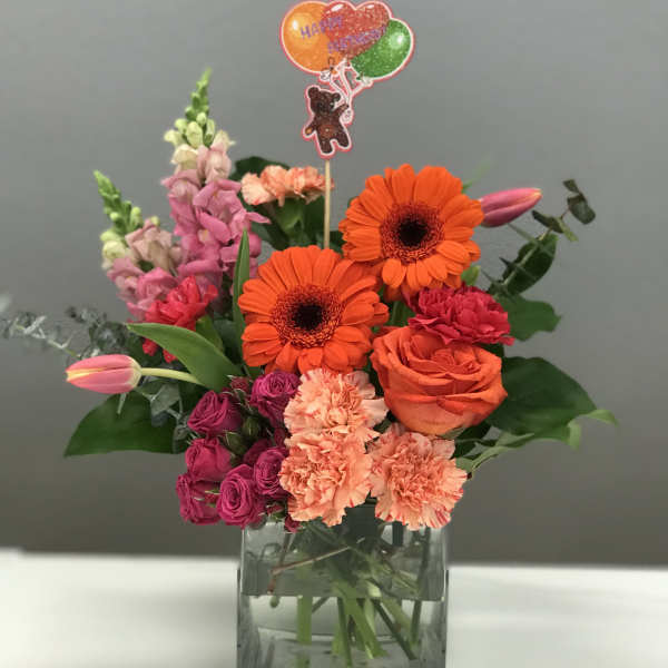Bright mixed bouquet in a square glass vase with a balloon topper