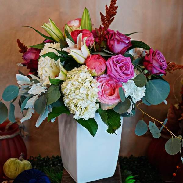 Tall white vase of pink roses, white hydrangeas, and lilies in a mixed arrangement