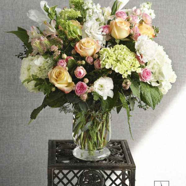 Mixed bouquet of roses, hydrangeas, and white blooms in a glass vase