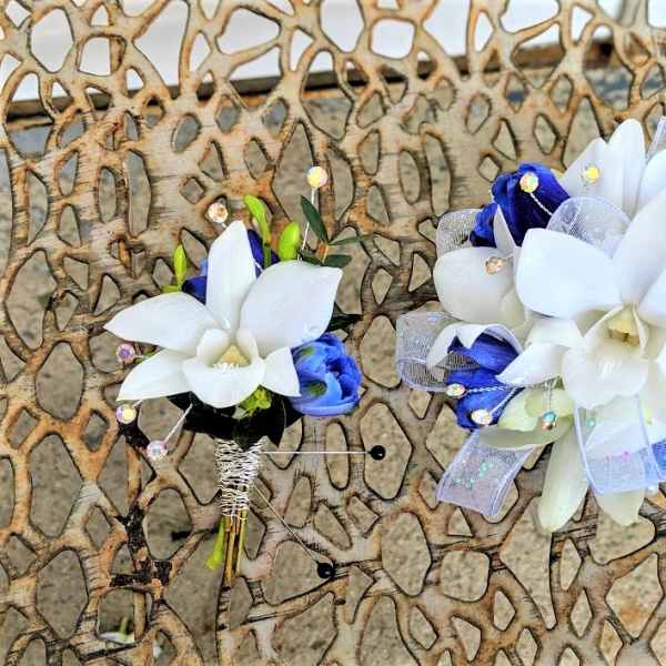 Two white and blue floral boutonnieres with ribbon accents