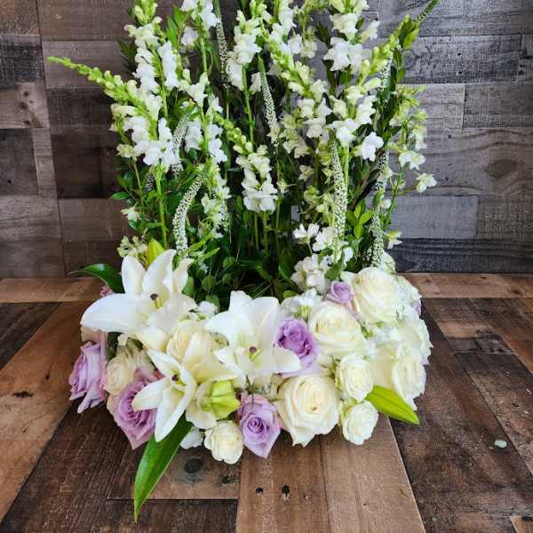 Tall white snapdragons with white lilies and ivory and lavender roses in a structured front-facing arrangement.