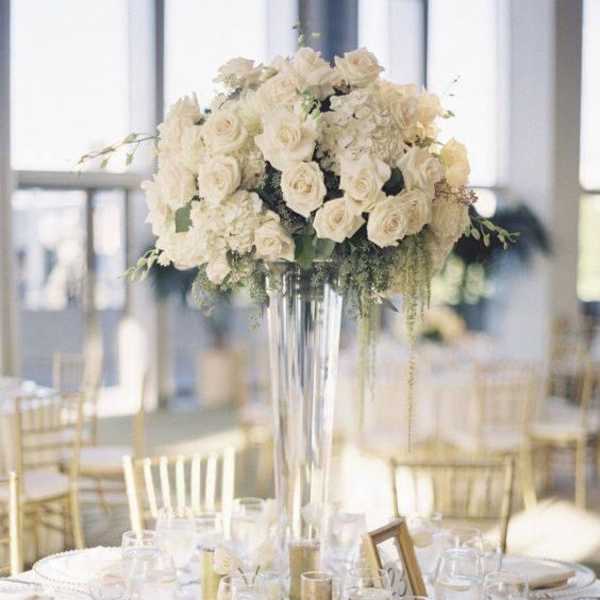 White rose centerpiece in a tall glass vase on a set dining table