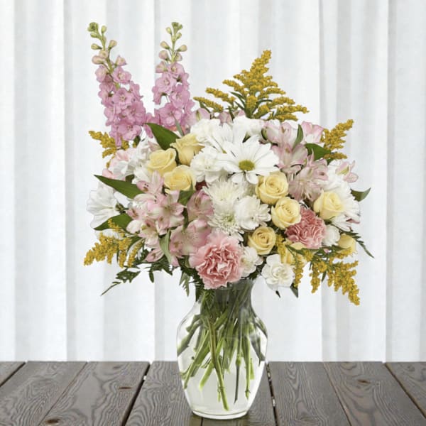 Mixed bouquet of pink, white, and yellow flowers in a clear glass vase
