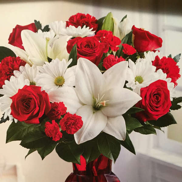Red roses, white lilies, and white daisies in a red glass vase