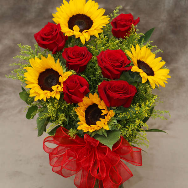Bouquet of red roses and yellow sunflowers in a glass vase with a red ribbon