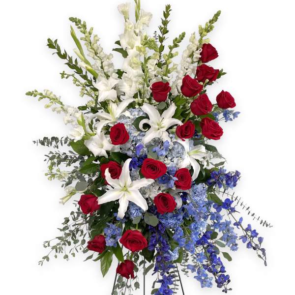 Tall standing arrangement of red roses, white lilies, and blue flowers on a metal easel