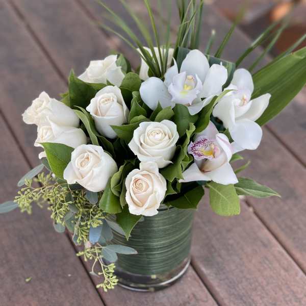 White roses and orchids arranged in a green tin container