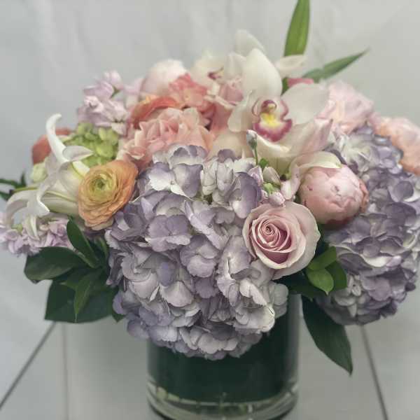Pastel bouquet of hydrangeas, roses, and orchids in a glass vase