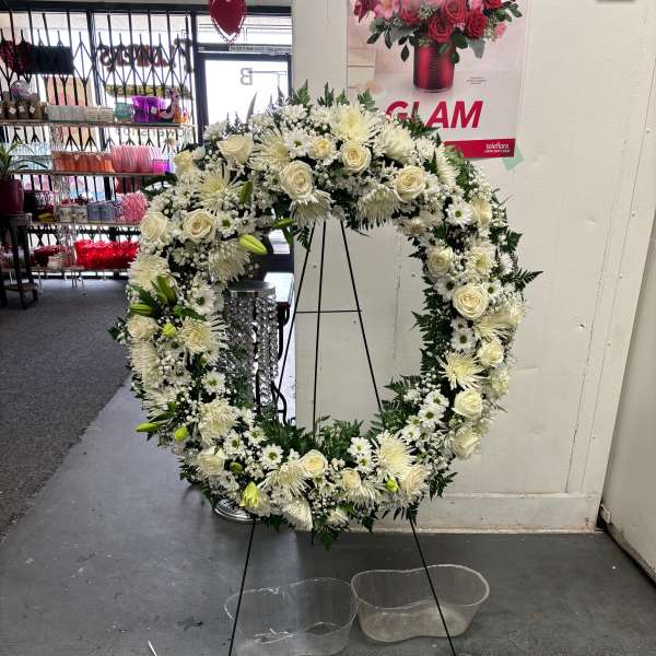 Large white floral wreath on a black stand with clear water basins below.