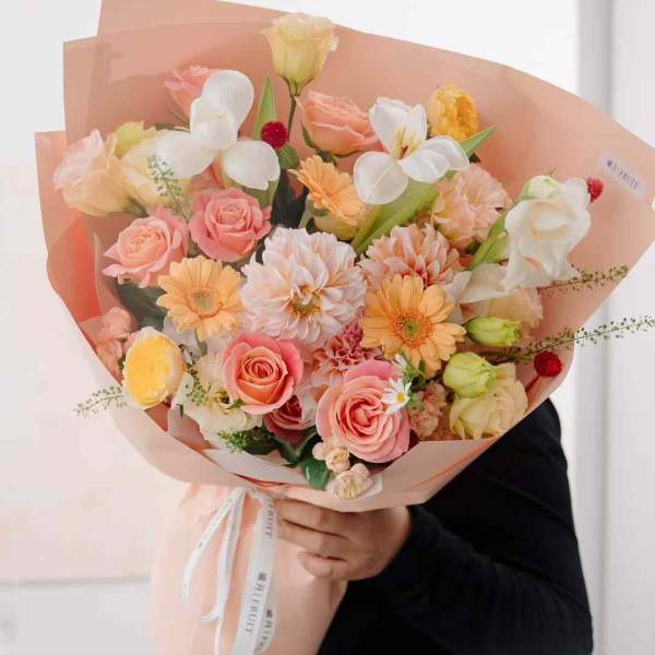 Large bouquet of pink, peach, and white flowers wrapped in peach paper