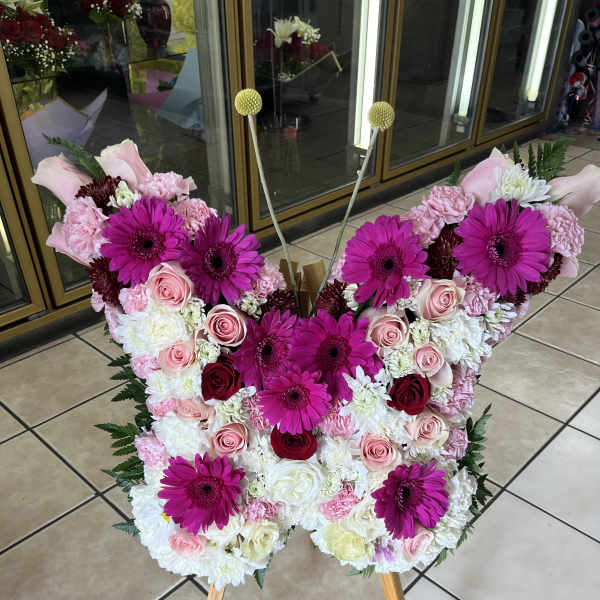 Standing butterfly-shaped floral display with pink gerbera daisies and roses on a wooden easel.